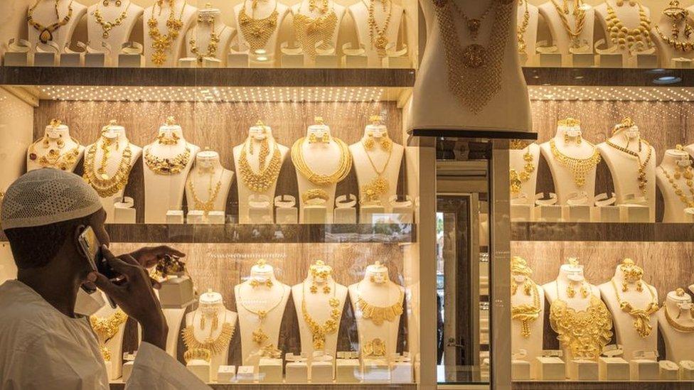 A man reaches for a gold ornament in a shop in a gold market.