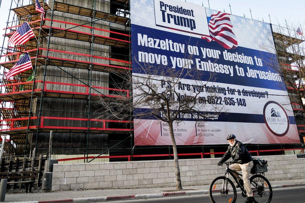 Man cycles past banner on a building in Jerusalem welcoming Donald Trump's plan to move the US embassy to Tel Aviv