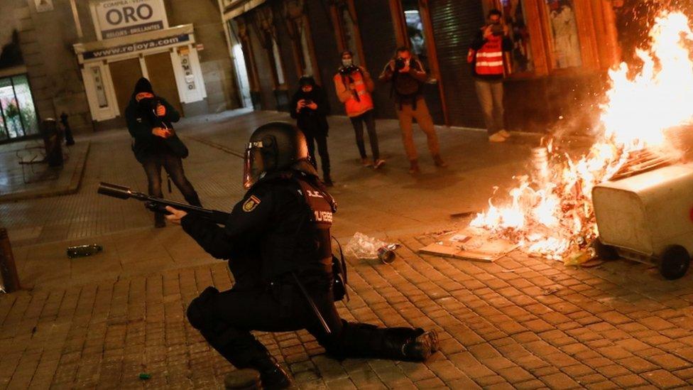 A police officer holds a gun as supporters of Catalan rapper Pablo Hasél protest against his arrest in Madrid, Spain