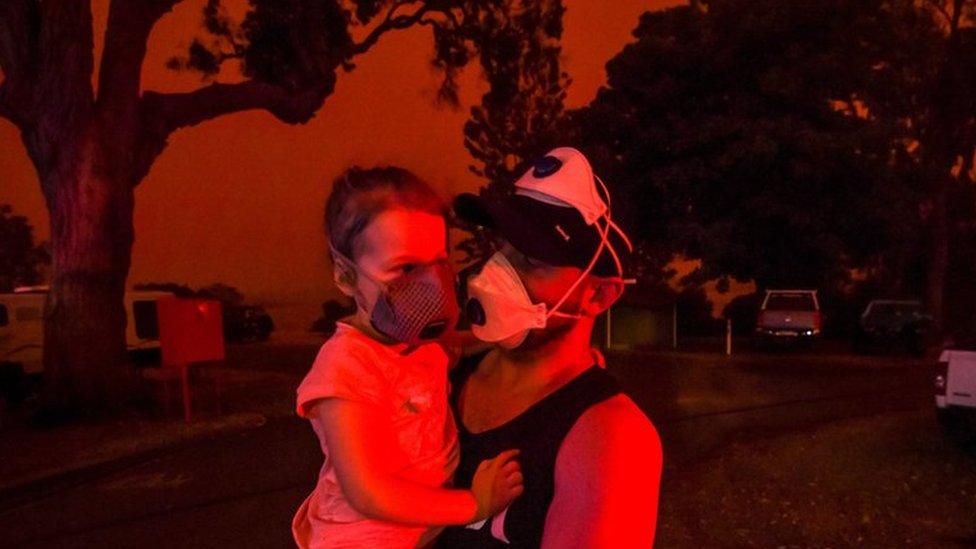 Mike hold his daughter Ella as the skies above turn red during the day on January 4, 2020 in Mallacoota, Australia