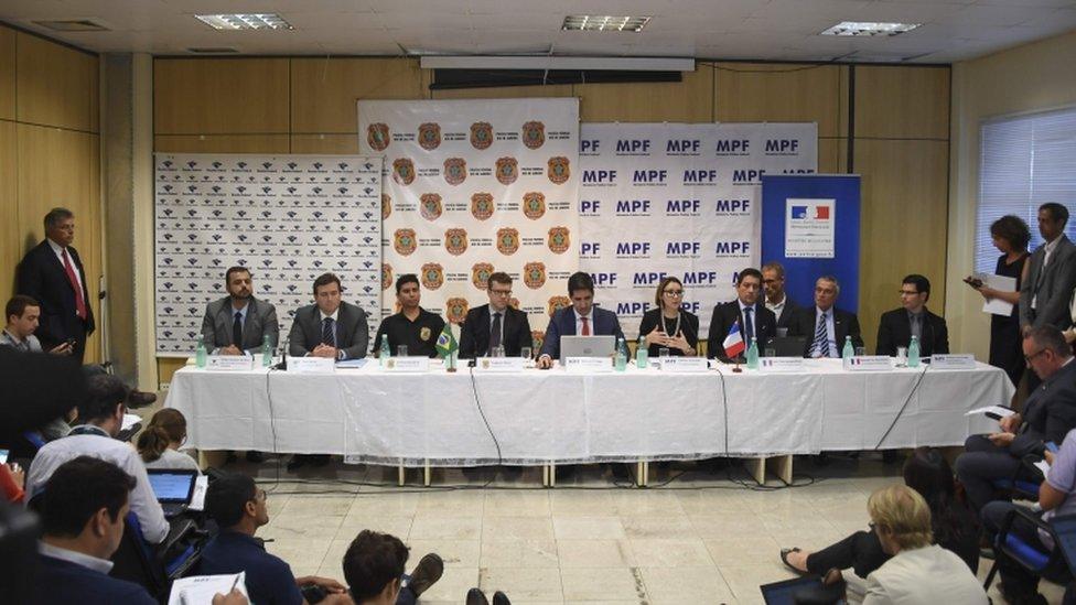 Members of French and Brazilian prosecution teams on corruption investigation appear at a table in front of news delegation.