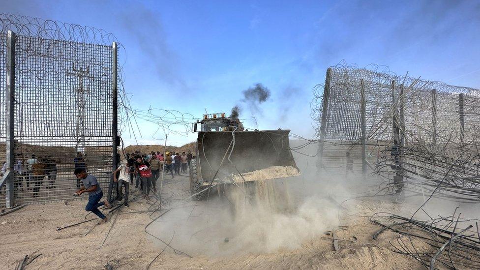 Palestinians groups break over a fence with the help of a digger as the clashes between Palestinian groups and Israeli forces continue in Gaza City, Gaza on October 7, 2023