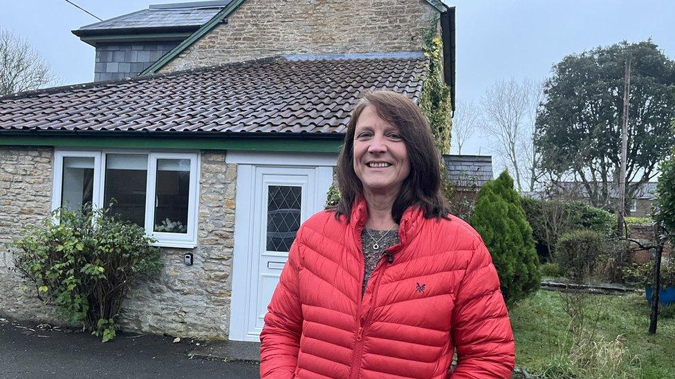 A woman in a red coat outside her rural home