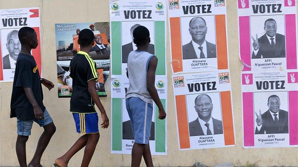 Boys walk past Ivory Coast's presidential election candidates campaign posters on October 14, 2015 in Cocody Abidjan.