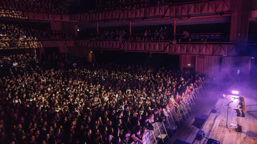 Holly Humberstone on stage at Bristol Beacon with a wide shot of a crowd in the background