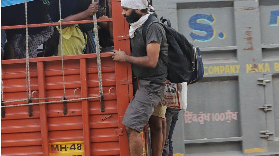 Two migrants hanging on the back of a truck