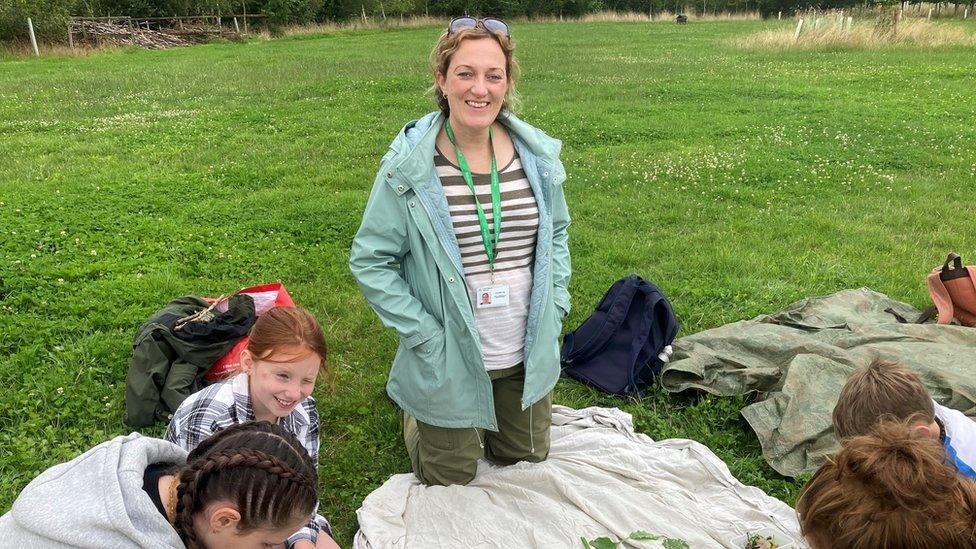 Jo Hiller-Culley Family and Parent Carer Worker for Carer Support Wiltshire kneeling in a field as young carers lay out items they have foraged from Jubilee Woods during a Carer Support Wiltshire summer activity run in collaboration with the Wiltshire Wildlife Trust