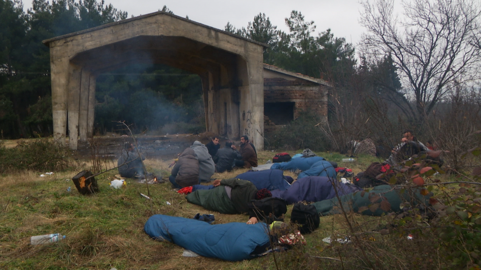 Migrant men lie in sleeping bags outdoors