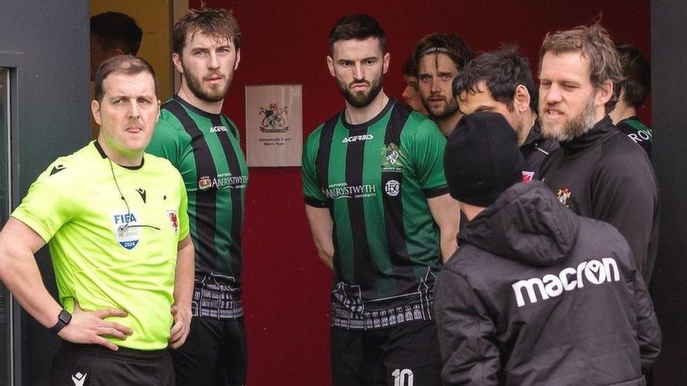 Match officials and Aberystwyth players wait for news at the USW Sport Park in Treforst