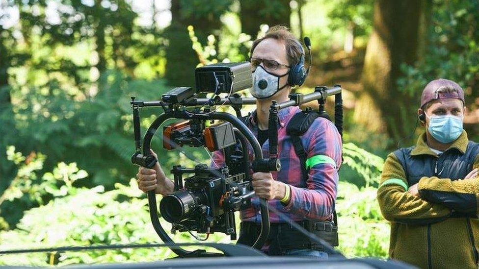 A camera operator wearing a mask holding a camera