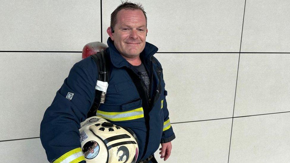 Ronnie Sherratt (short brown hair) with firefighters' protective clothing and helmet