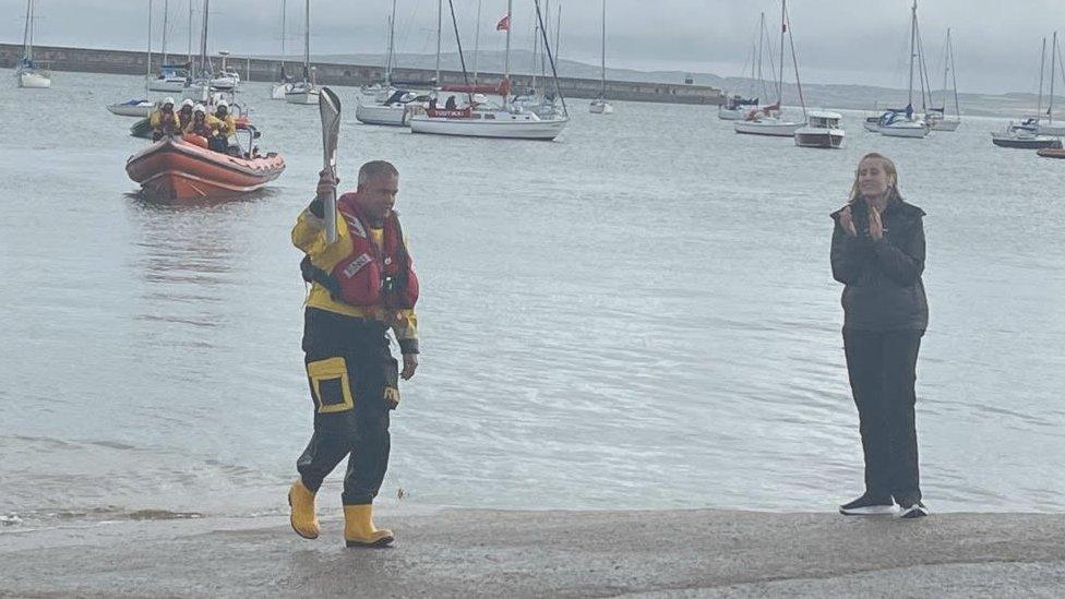 Marc Falloon o'r RNLI yn dod â'r baton i'r lan