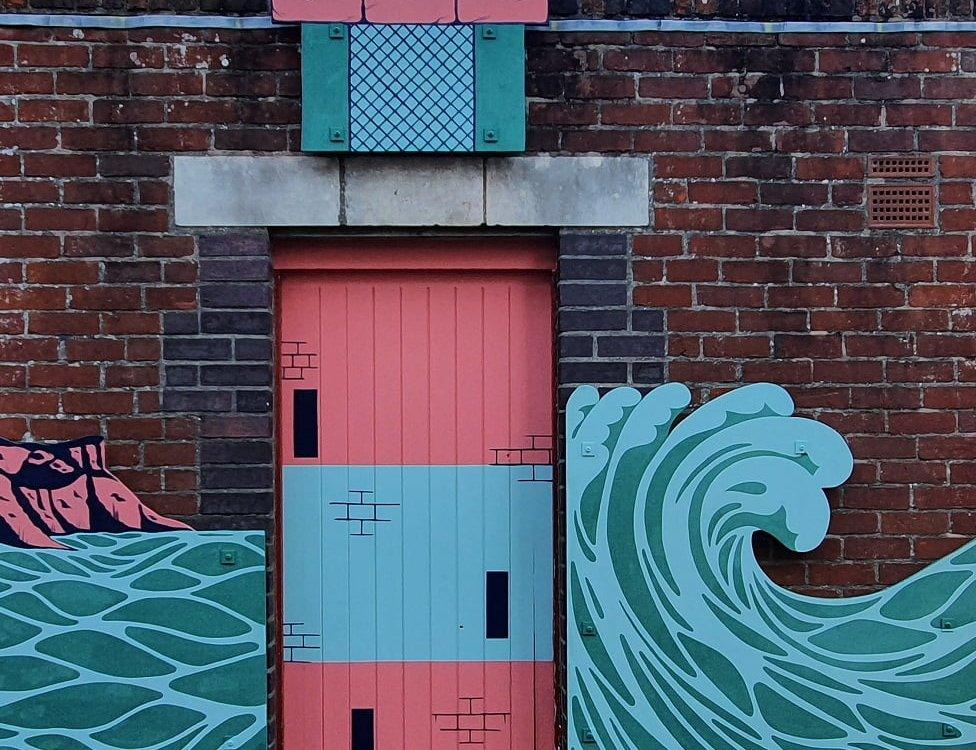 Sea waves mural on a brick wall incorporating a door which has been painted to look like a lighthouse