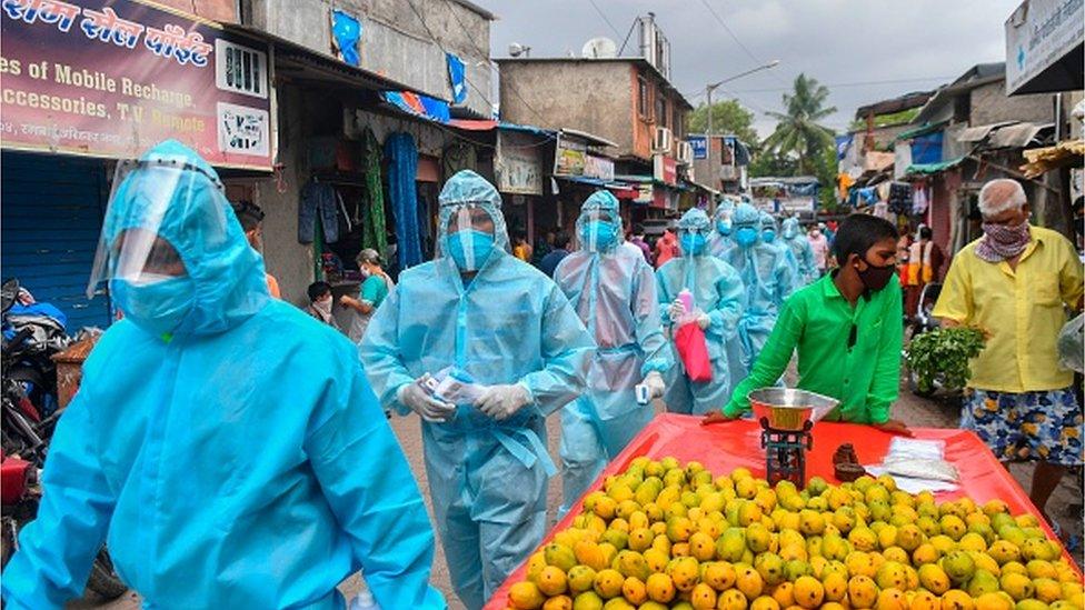 Medical staff wearing Personal Protective Equipment (PPE) gear walk through a market for a door-to-door screening inside a Mumbai slum