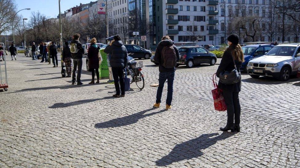 People line up in front of an organic grocery store in Berlin, Germany, 24 March 2020