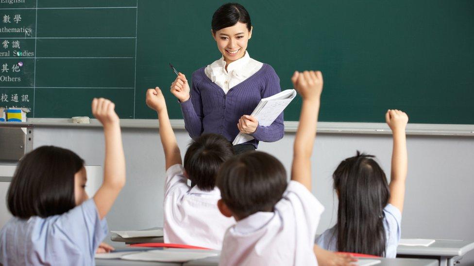 Students In A Chinese School Classroom Putting Up Their Hands To Answer The Teacher