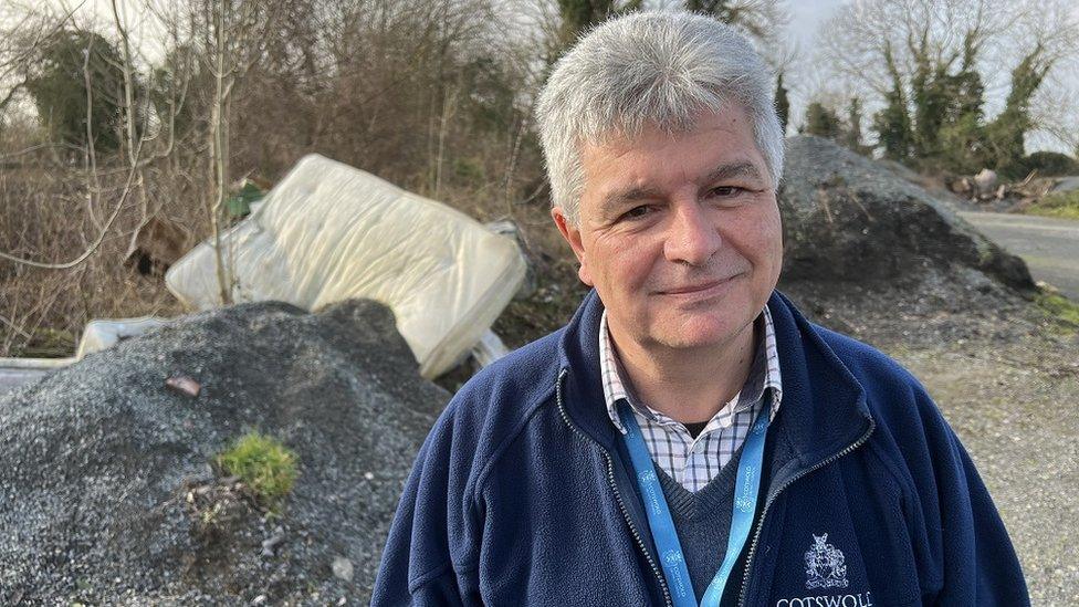 Kevin Lee stands in front of a fly-tipped mattress looking at the camera wearing council branded gear