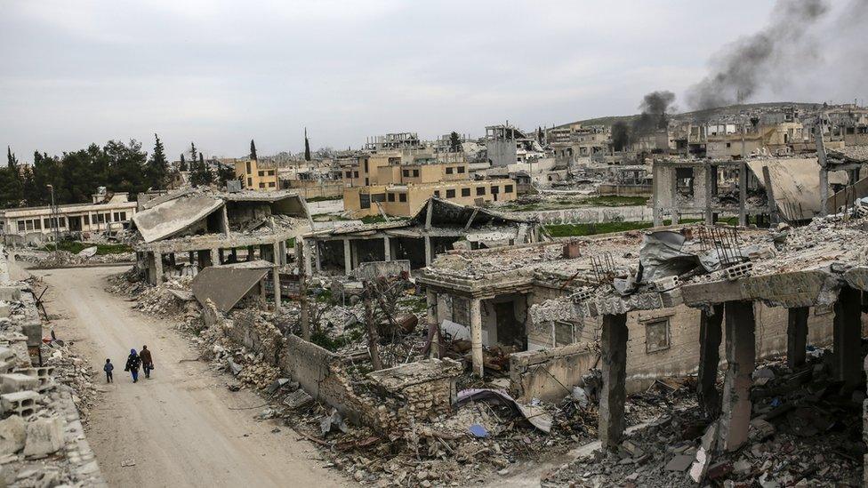 People walk along a conflict damaged street in the Syrian town of Kobane in March 2015