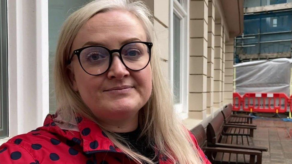 Amy Freeman wears glasses and a red polka dot coat and looks at the camera