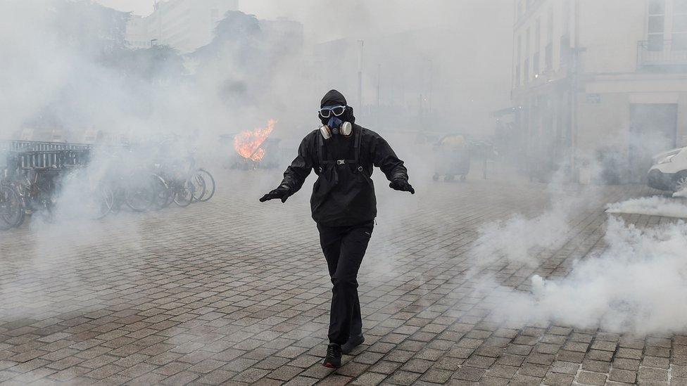 A protester dressed in black walks amid tear gas smoke during a protest against the pension overhauls, in Nantes, on 5 December, 2019.