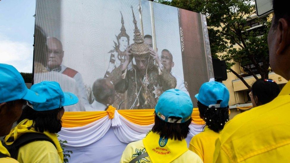 Volunteers watch the crowning of King Maha Vajiralongkorn during the Royal Coronation,