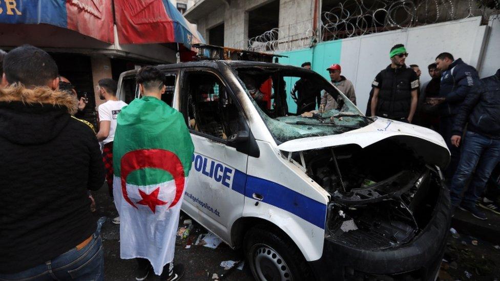 Protesters stand near a burnt-out police van in Algiers, April 2019