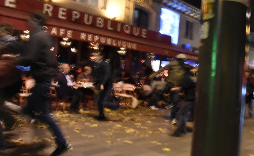 People sitting outside a cafe as people run past after a shooting in Paris