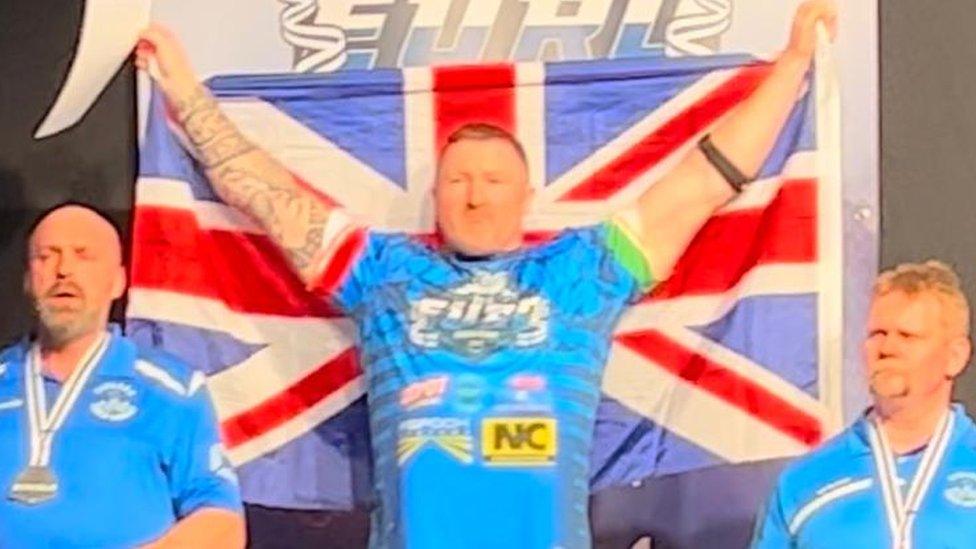 Mark Waldon on a podium with a British flag after winning a European arm wrestling title