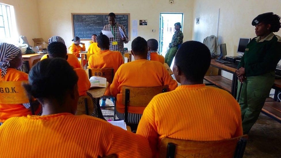 Inmates wearing orange and listening to a teacher in a classroom