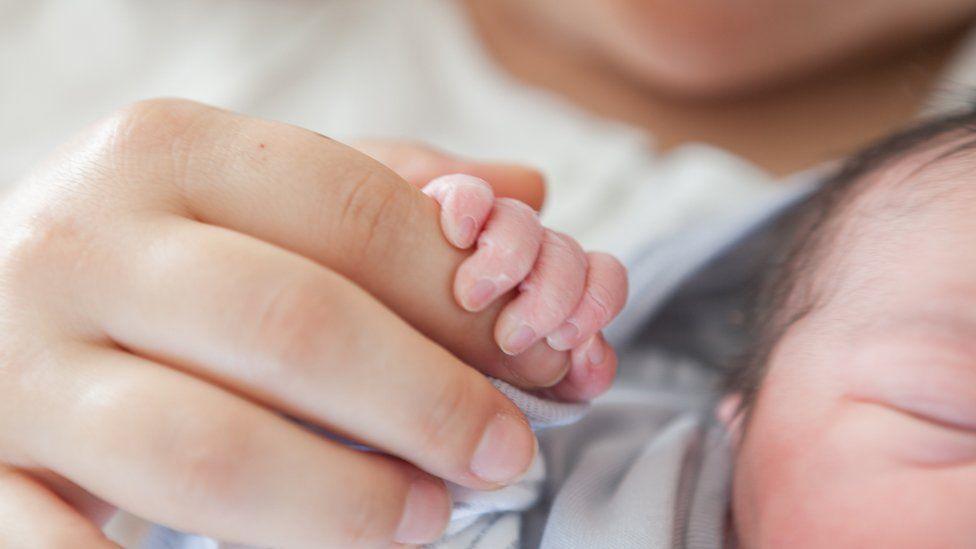 Llaw mam yn cydio ym mysedd ei babi newydd-anedig