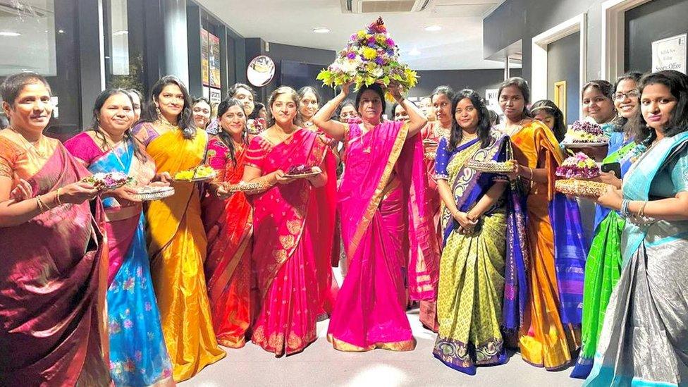 Women in colourful sarees holding a flower stack