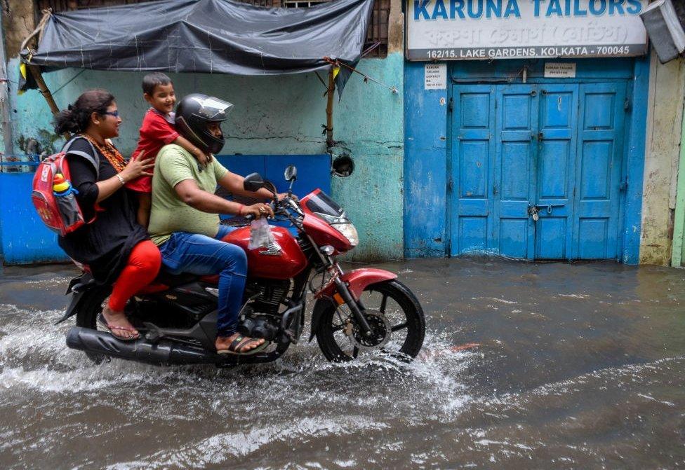 A family is seen making their way through a flooded street in Kolkata , India , on 2 August 2023 . Overnight rain caused many parts of Kolkata to be waterlogged , causing chaos during peak office hour of the day.