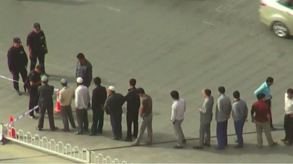 A line of local men waiting in line to be searched by the police