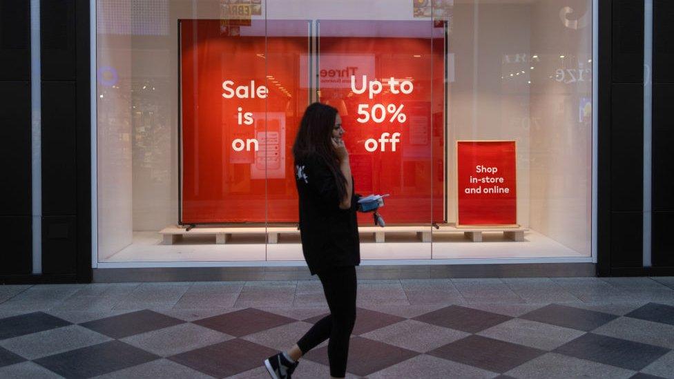 Woman walks past shop advertising discount in Oxford