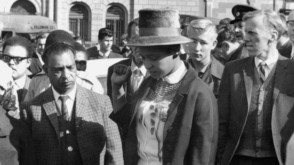 Winnie Mandela (C), leaves the Palace of Justice in Pretoria 16 June 1964 with her fist clenched, after the verdict of the Rivonia Trial was given, sentencing eight men, including her husband anti-apartheid leader and African National Congress (ANC) member Nelson Mandela, to life imprisonment