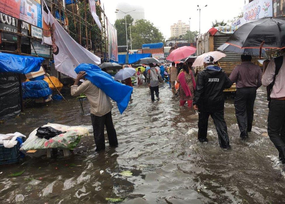 People trying to navigate the streets flooded with rain, umbrellas at hand.