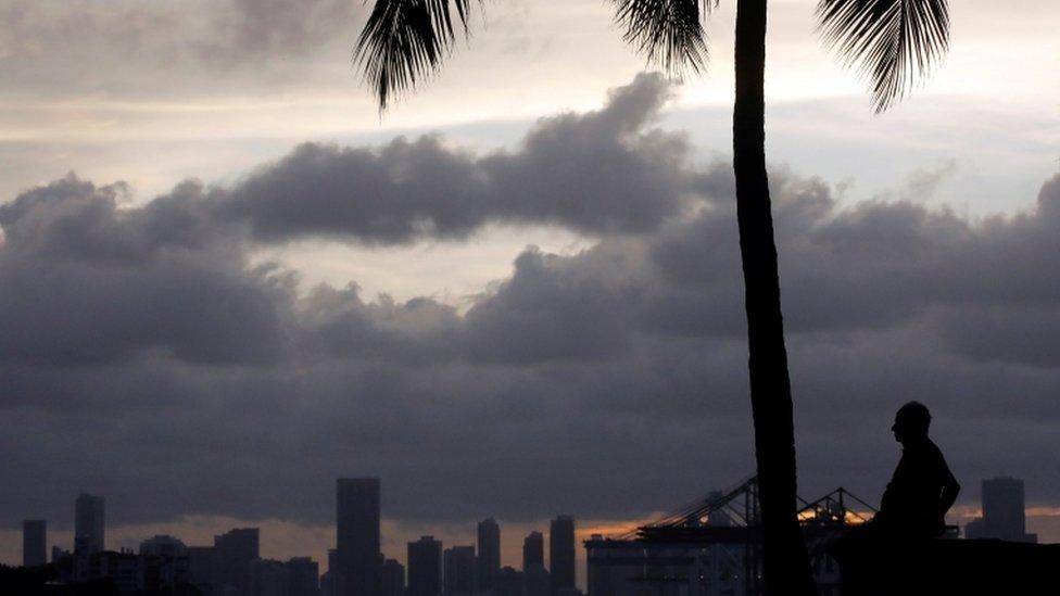 A silhouette of a man and a palm tree with Miami skyline and clouds behind him