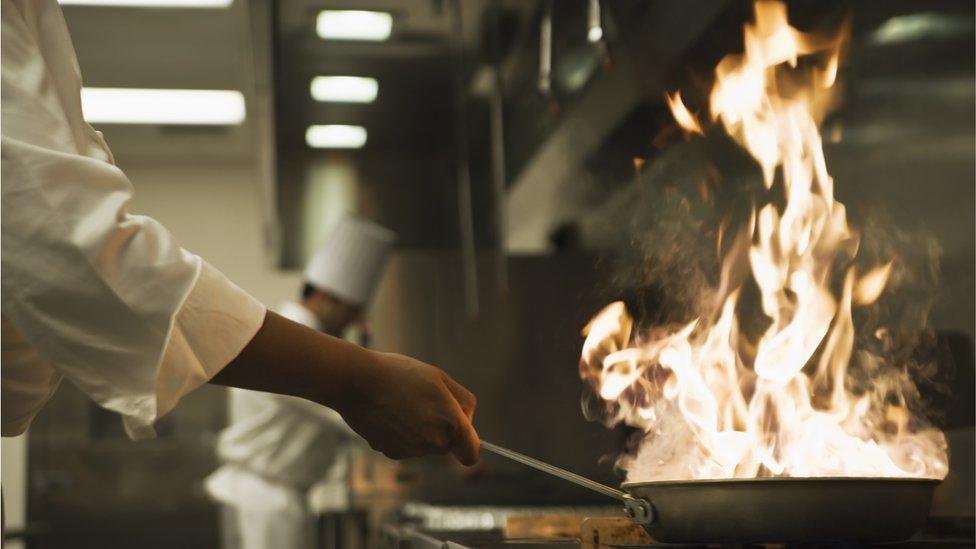 A chef is close to a hot flame from a pan
