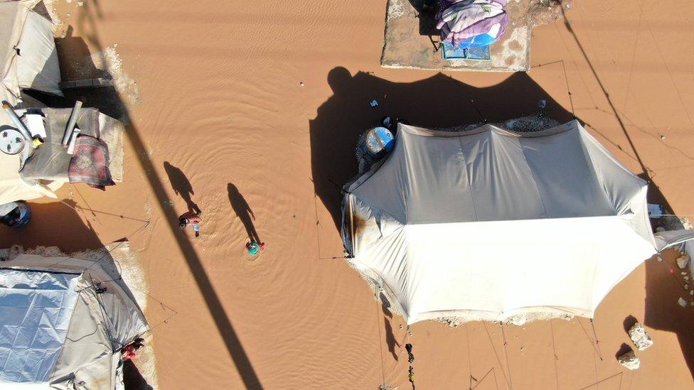 A girl and a boy stand next to their flooded tent at a camp in northern Idlib province, Syria