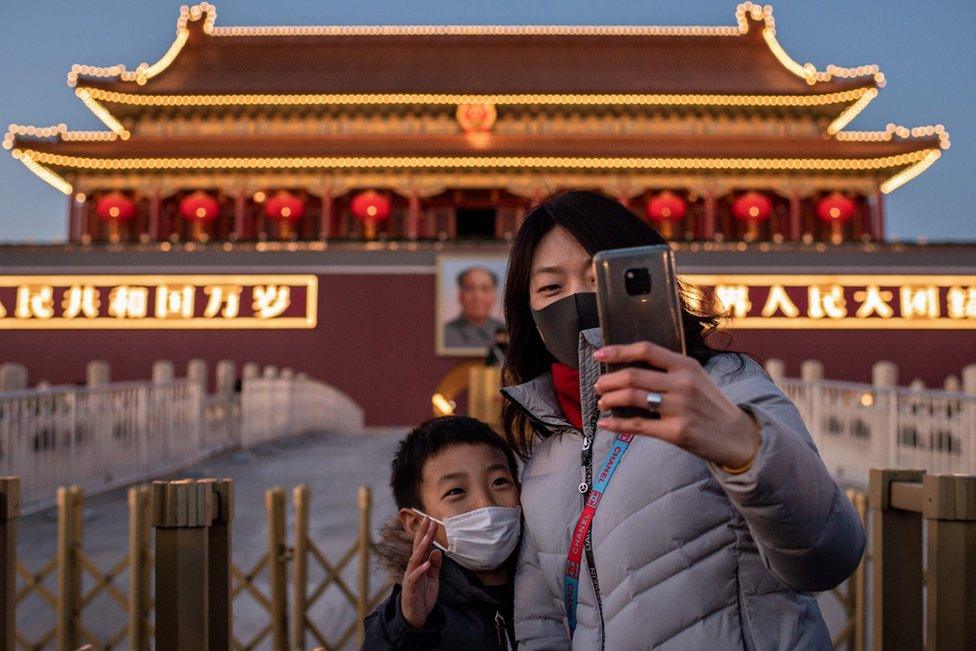 A woman and a boy wearing protective masks take a selfie in front of a portrait of late communist leader Mao Zedong at Tiananmen Gate in Beijing.