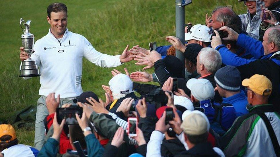 2015 Open winner Zach Johnson holds the Claret Jug trophy in front of golf fans