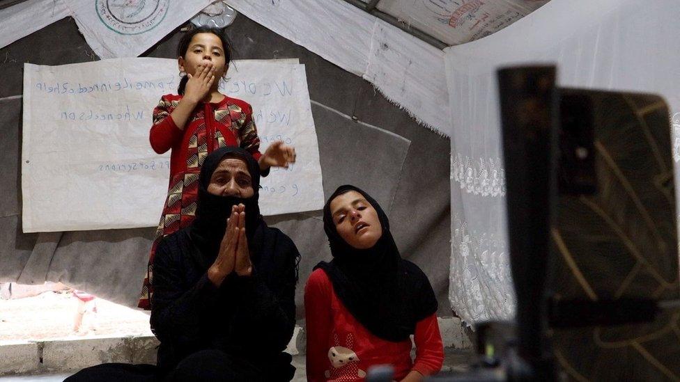 A woman and her young daughters pictured begging in front of a smartphone livestream