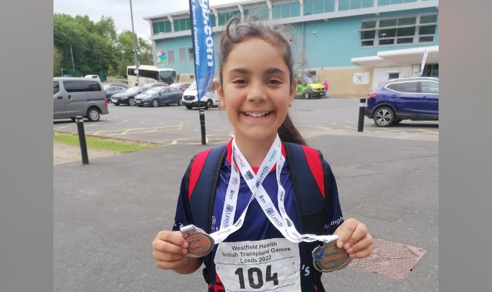 A girl smiling holding medals won at the British Transplant Games