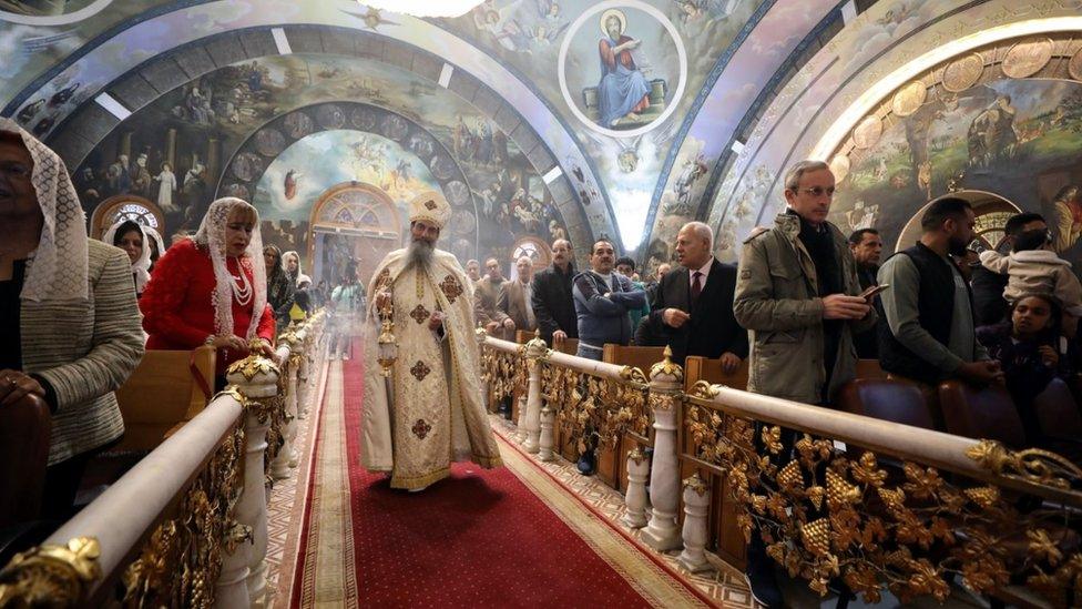 A Coptic Orthodox clergyman walks past worshippers during a mass at an Orthodox church during Christmas eve