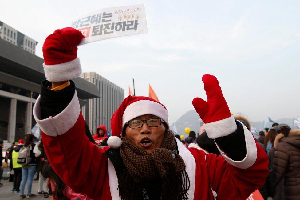 A South Korean wearing a Santa Claus costume, shouts slogans while carrying placard reading "Park Geun-Hye and Prime Minister Hwang Kyo-ahn Out" during a rally against president Park Geun-hye on the Gwanghwamun Square in Seoul, South Korea, 24 December 2016.