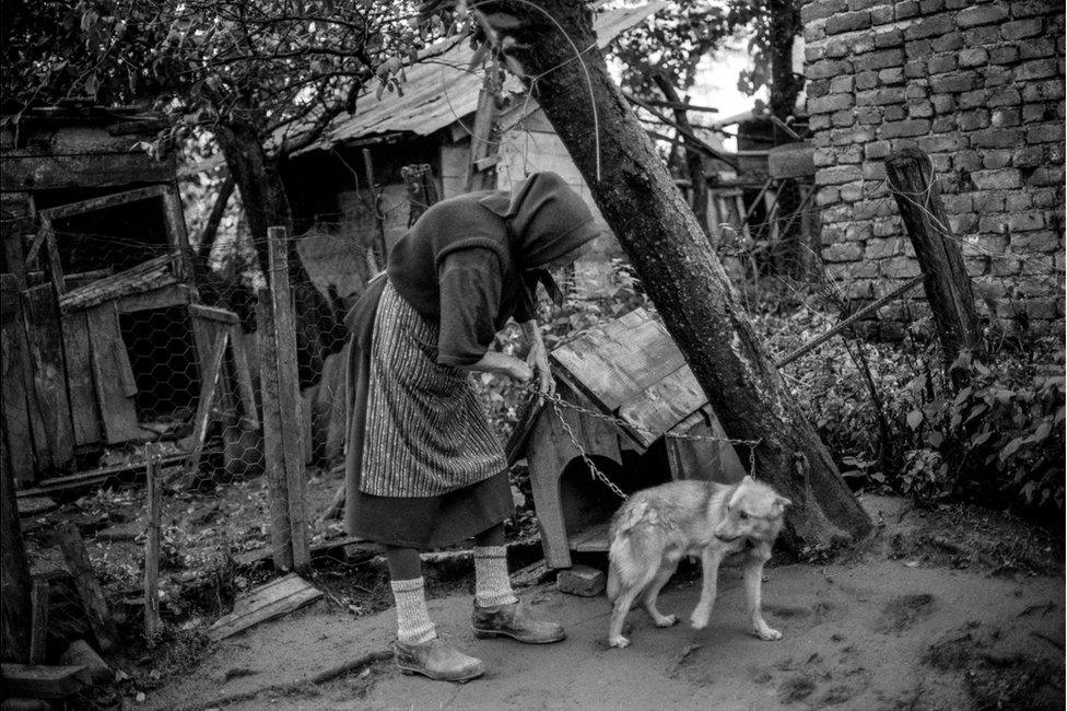 An elderly woman holds the chain of her dog next to her