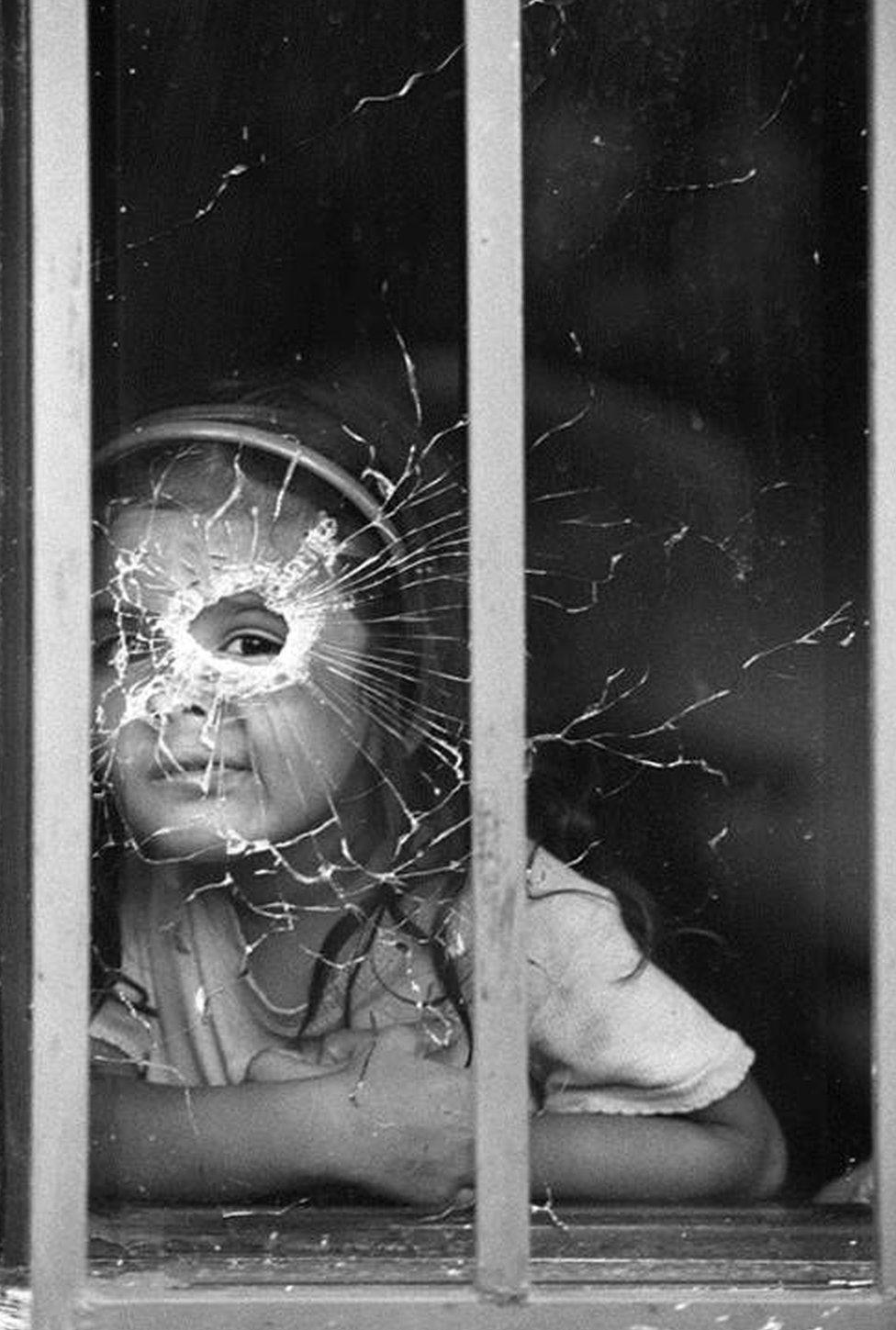 Girl looking through bullet-shattered window