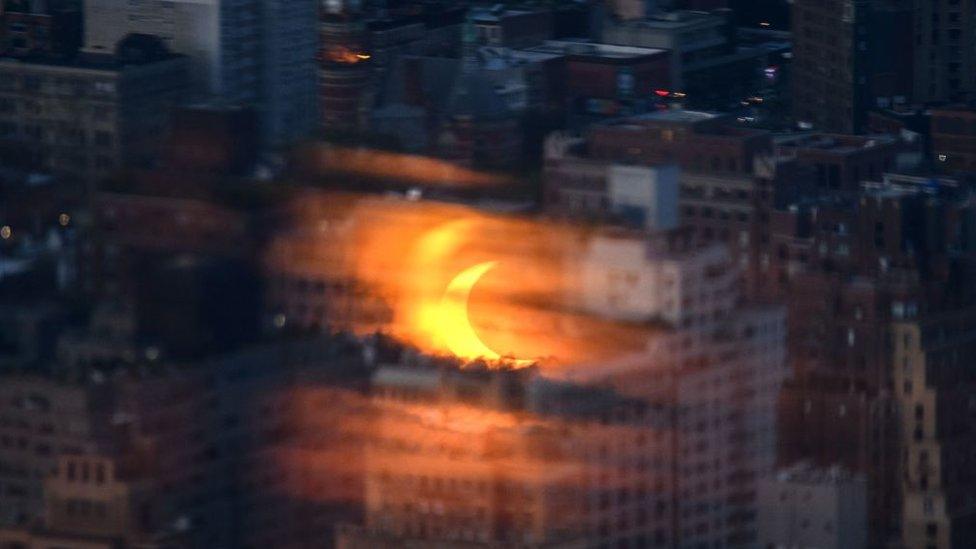 Partial solar eclipse is reflected on a glass panel before buildings of the Manhattan skyline.