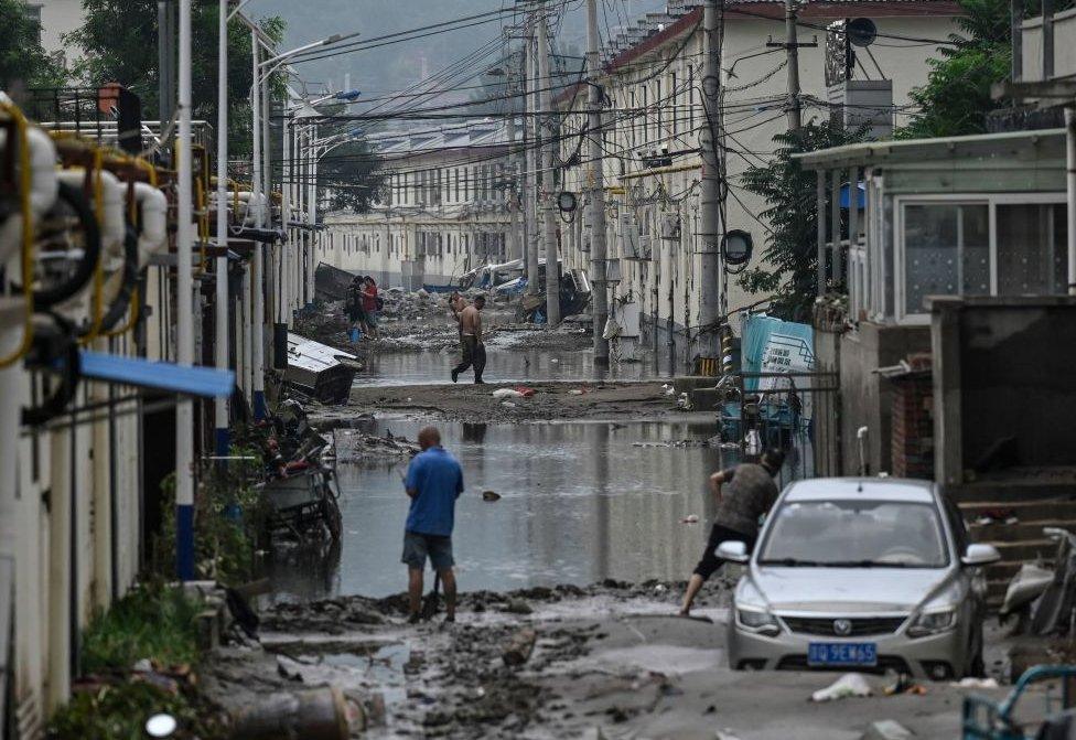 Residents clean up the street in the aftermath of the flooding at a village following heavy rains in Beijing on August 3, 2023.