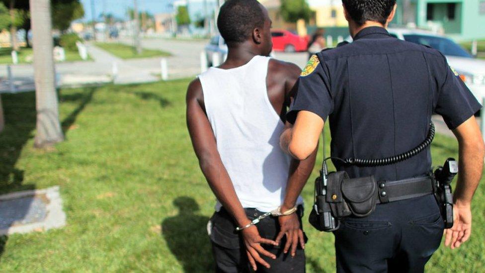 A police officer walks a handcuffed person to a patrol car in Miami, Florida - 11 August 2010